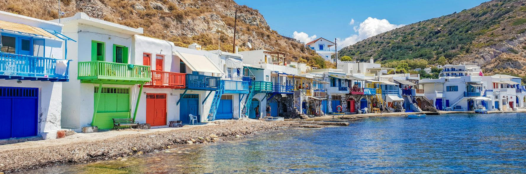 Colorful houses along a waterfront with clear blue water and mountains in the background