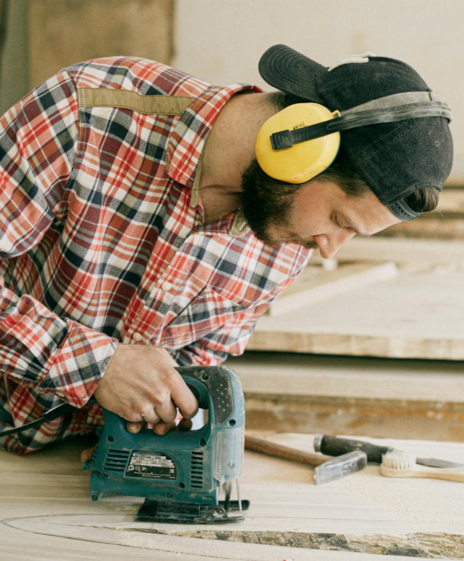 Person using a jigsaw on a wooden surface with tools around