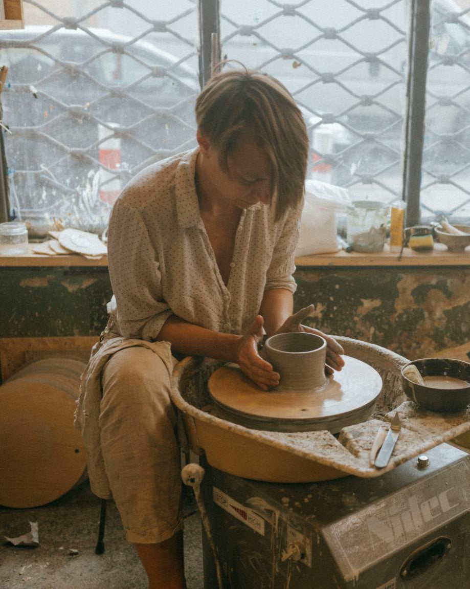 Person working with clay on a pottery wheel in a studio setting.