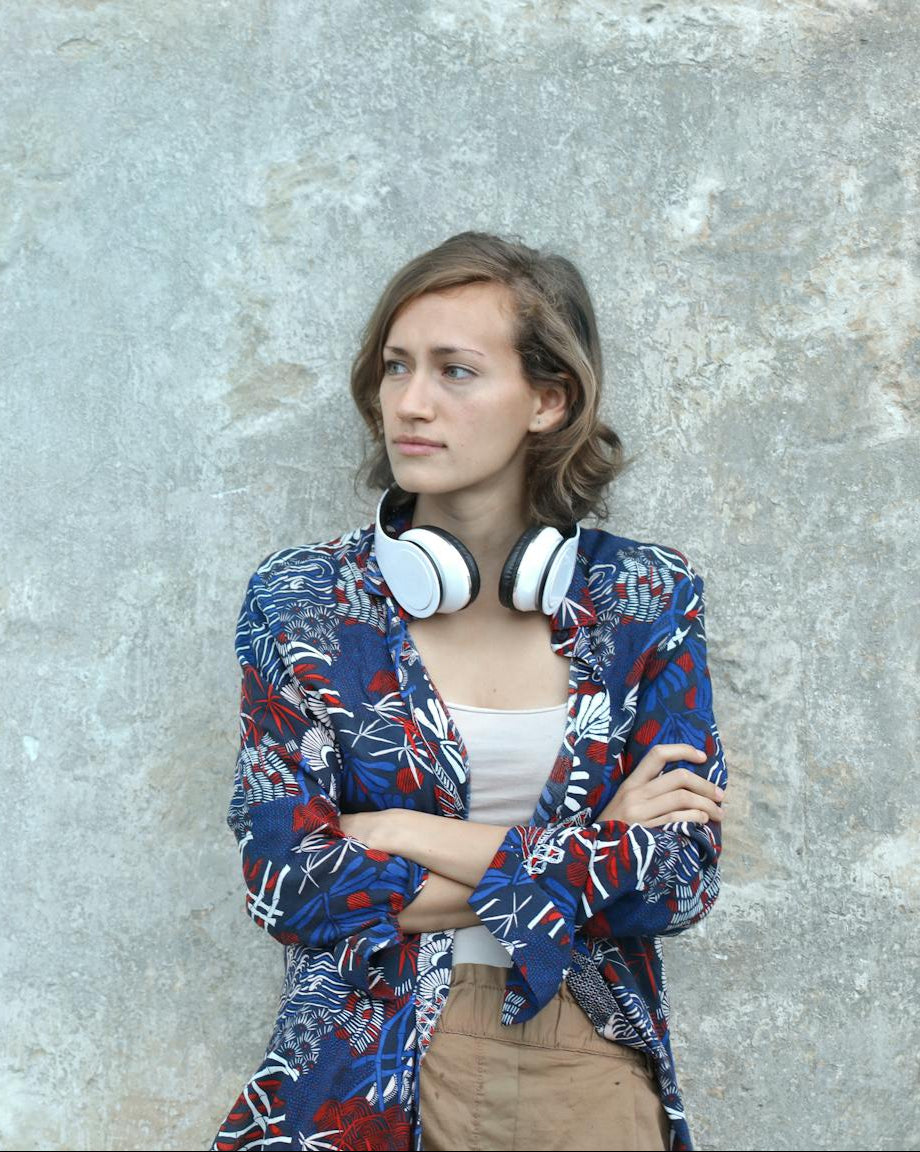 Woman wearing a colorful jacket and headphones against a textured wall.
