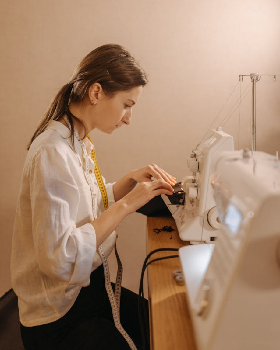 Woman working on a sewing machine with a beige wall in the background