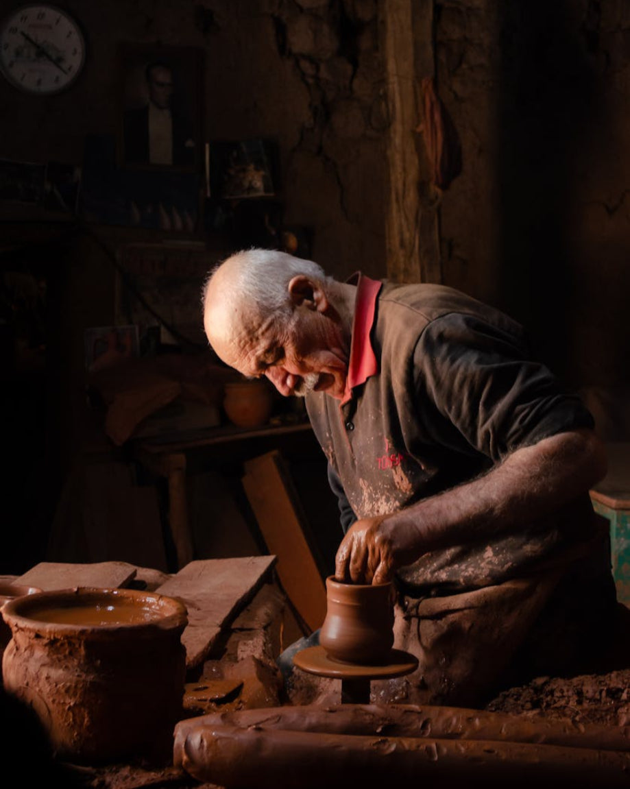 Man working with clay on a potter's wheel in a dimly lit workshop.