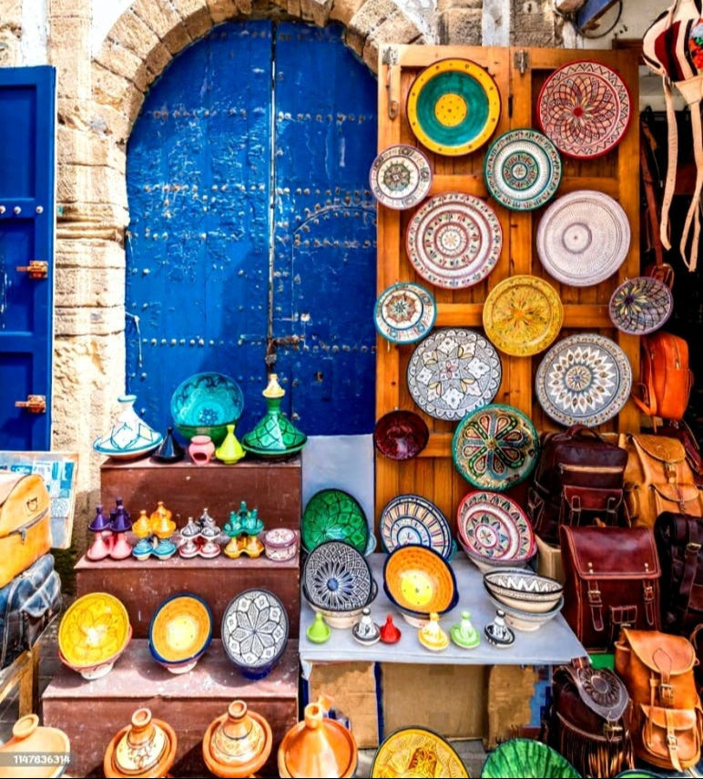 Colorful ceramic plates and pots displayed in front of a blue door in a traditional market setting.