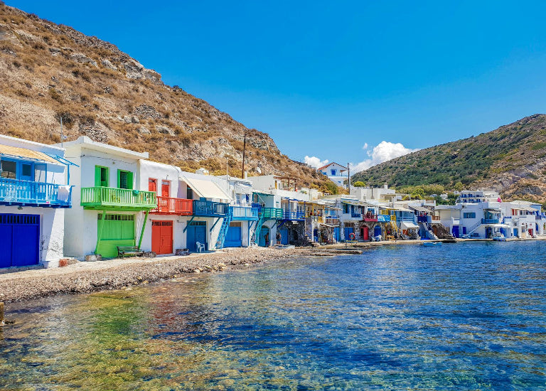Colorful houses along a waterfront with clear blue water and mountains in the background