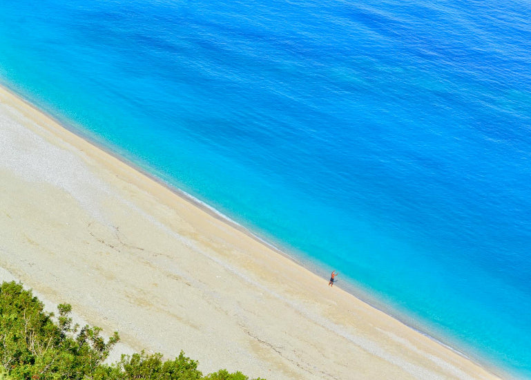 Beach with clear blue water and a person standing on the sand