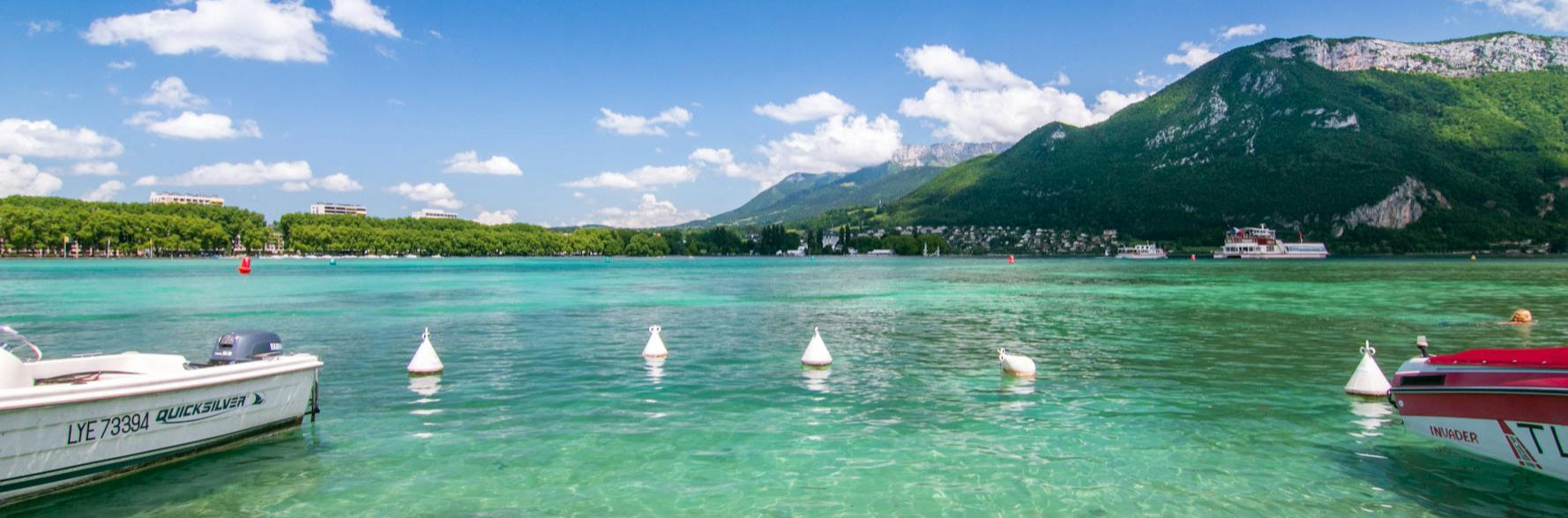 Clear turquoise lake with boats and green mountains under a blue sky.