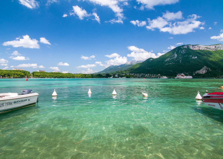 Clear turquoise lake with boats and green mountains under a blue sky.