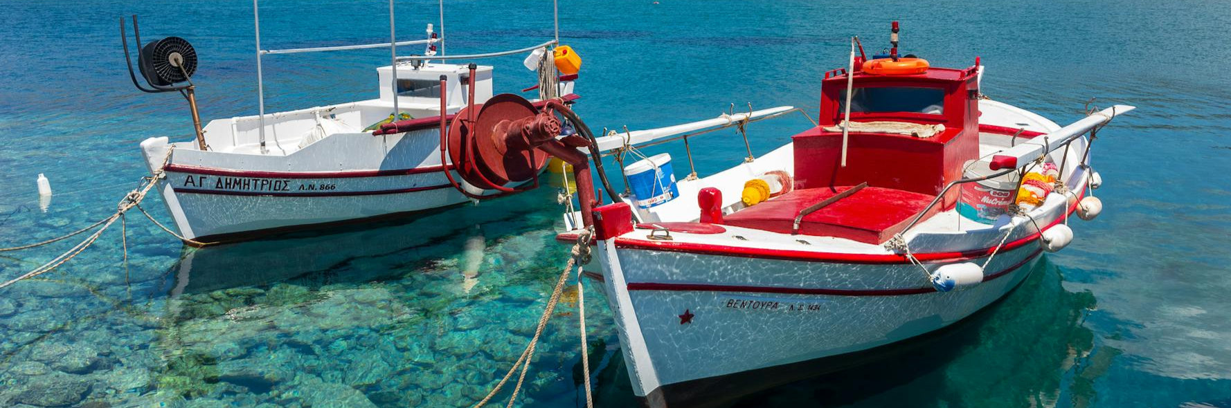 Two boats docked in clear blue water with a scenic background