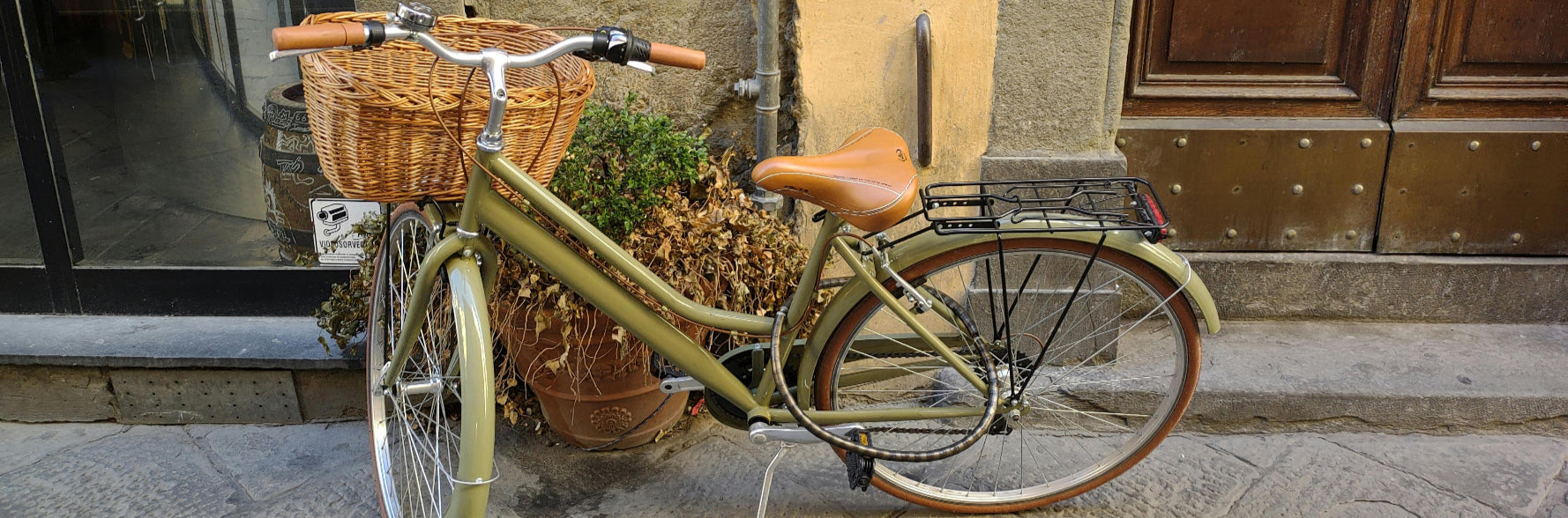 Vintage bicycle with a basket on a stone pavement in front of a building entrance.