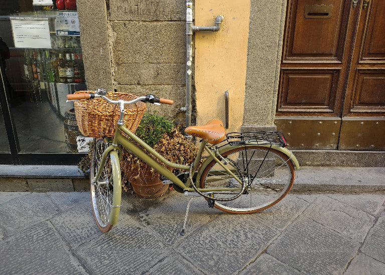Vintage bicycle with a basket on a stone pavement in front of a building entrance.