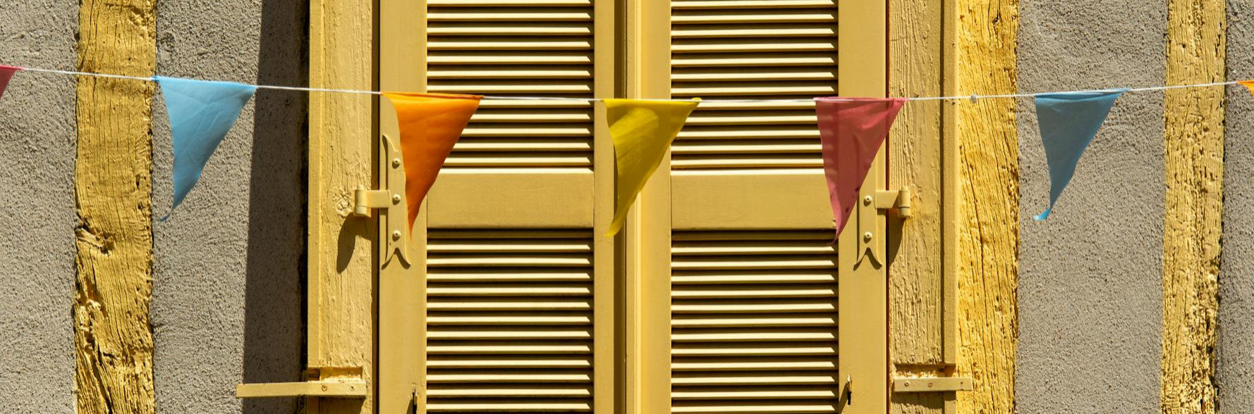 String of colorful triangular flags in front of a yellow shutter.