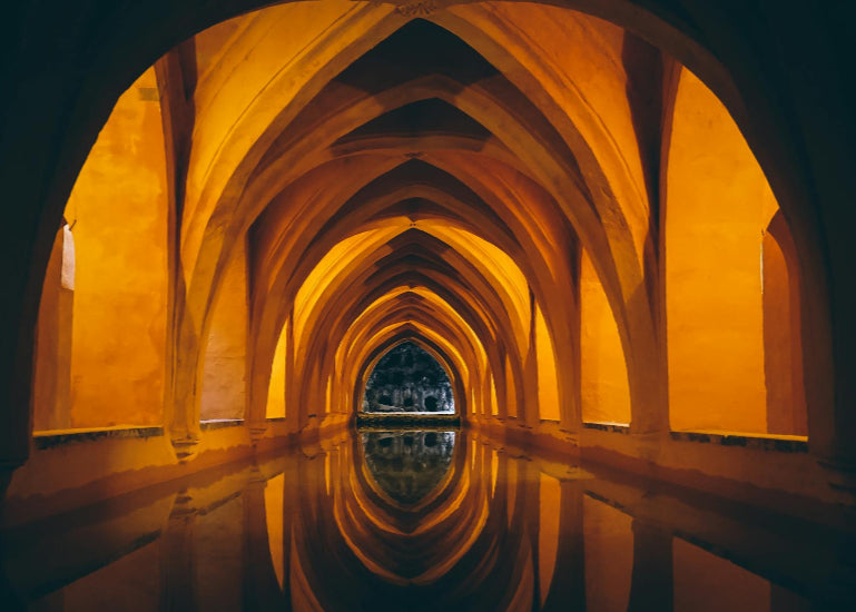 Long, narrow tunnel with arches reflecting in water at night