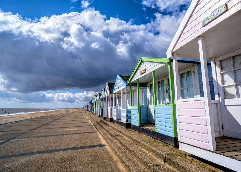 Colorful beach huts along a sandy promenade with a cloudy sky.