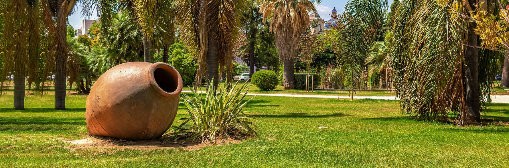 Large clay pot in a park with palm trees and clear blue sky